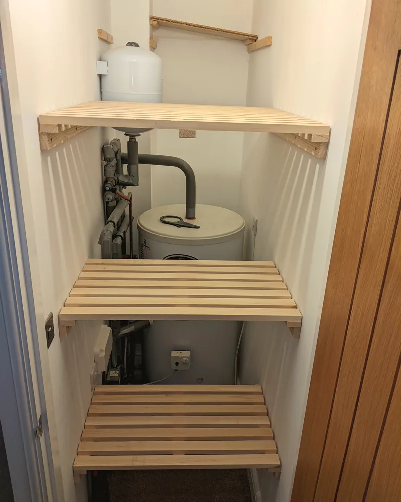 Airing cupboard fitted with slatted timber shelves around the cylinder