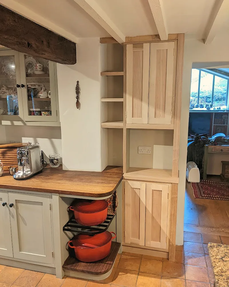 Built-in shelving and cupboards fitted into a cottage alcove beside an exposed beam