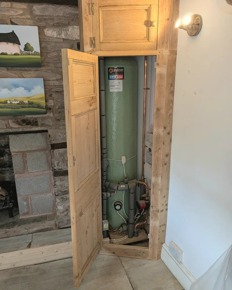 Pine cupboard built to enclose a hot water cylinder in a stone-walled room