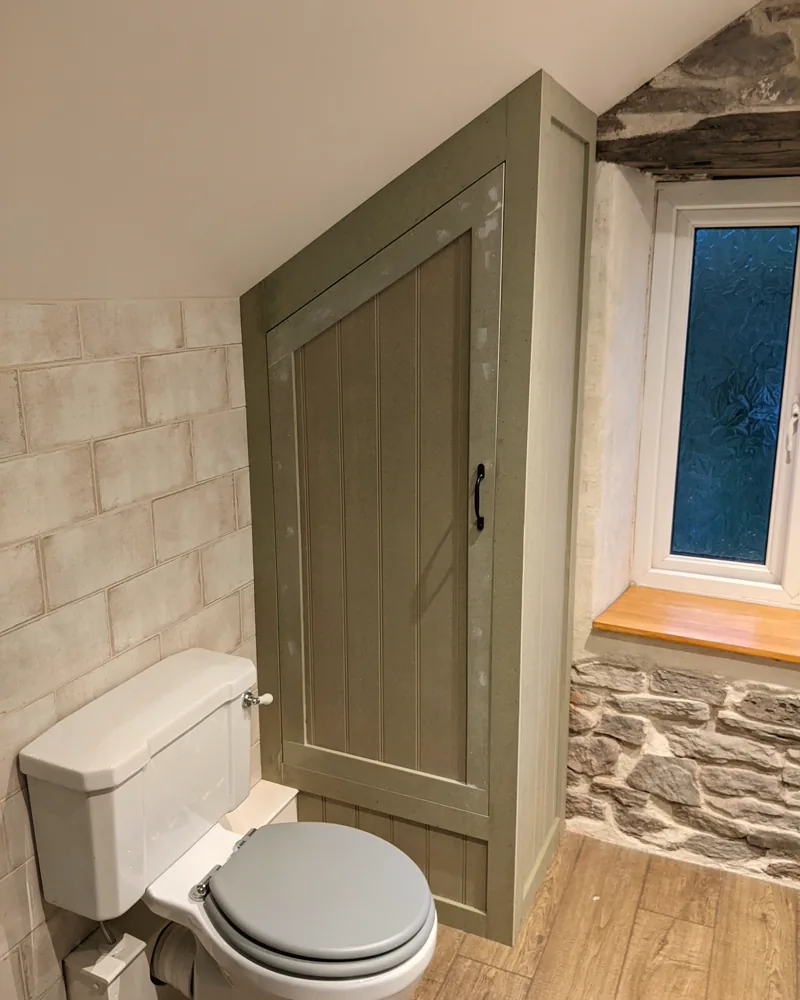 Sage green cupboard fitted under the eaves in a stone-walled bathroom