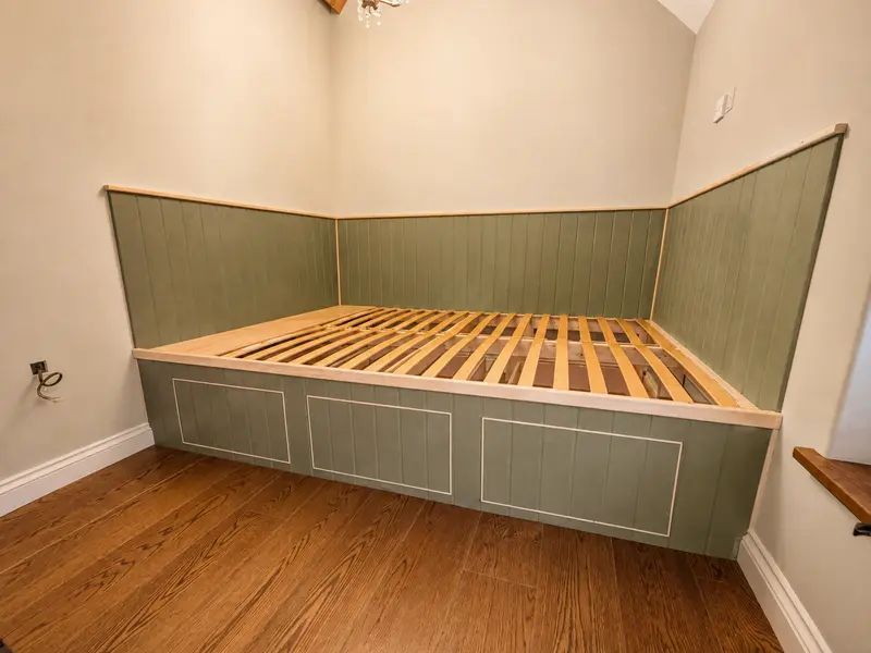 Sage-panelled fitted bed frame with drawer storage, built into a panelled corner