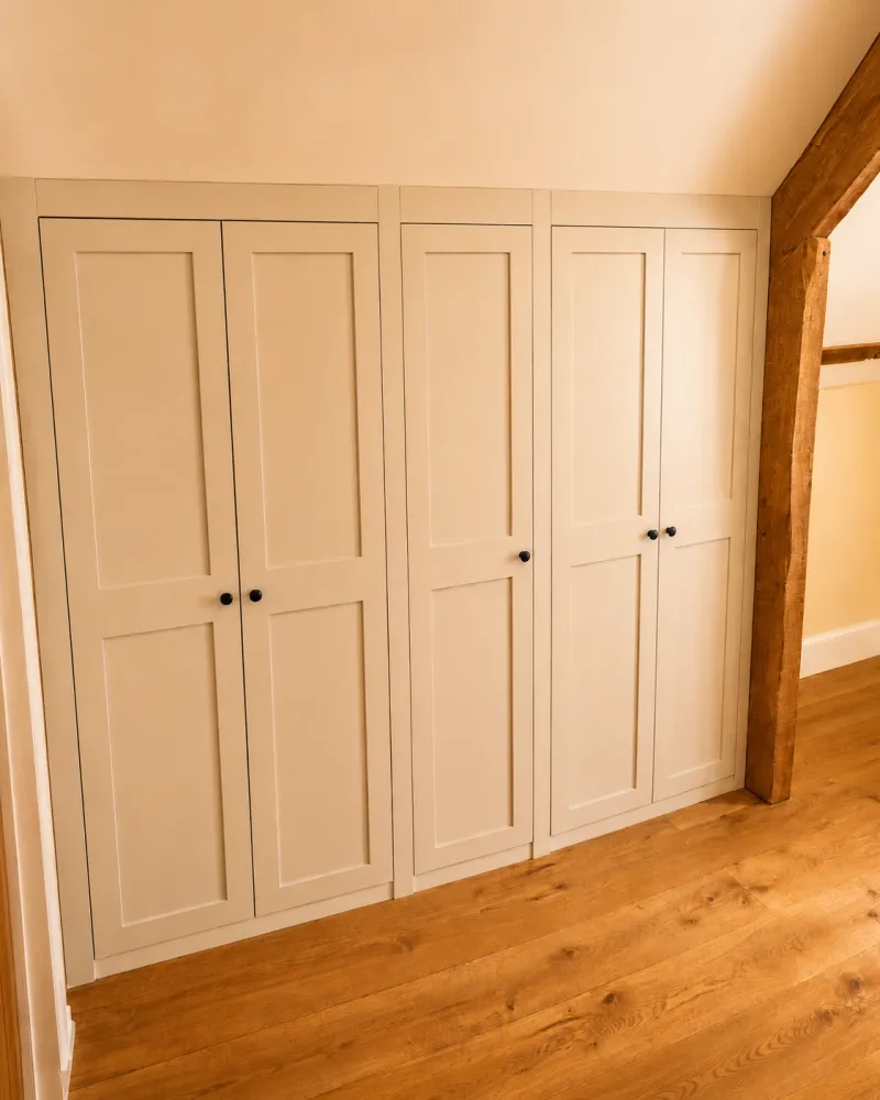 Fitted wardrobes built into a loft bedroom, scribed to the sloping ceiling beside an exposed beam