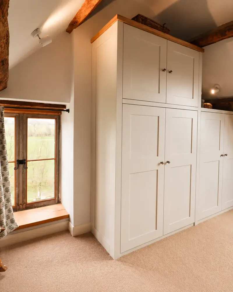 Fitted wardrobes built between exposed beams under a sloping ceiling