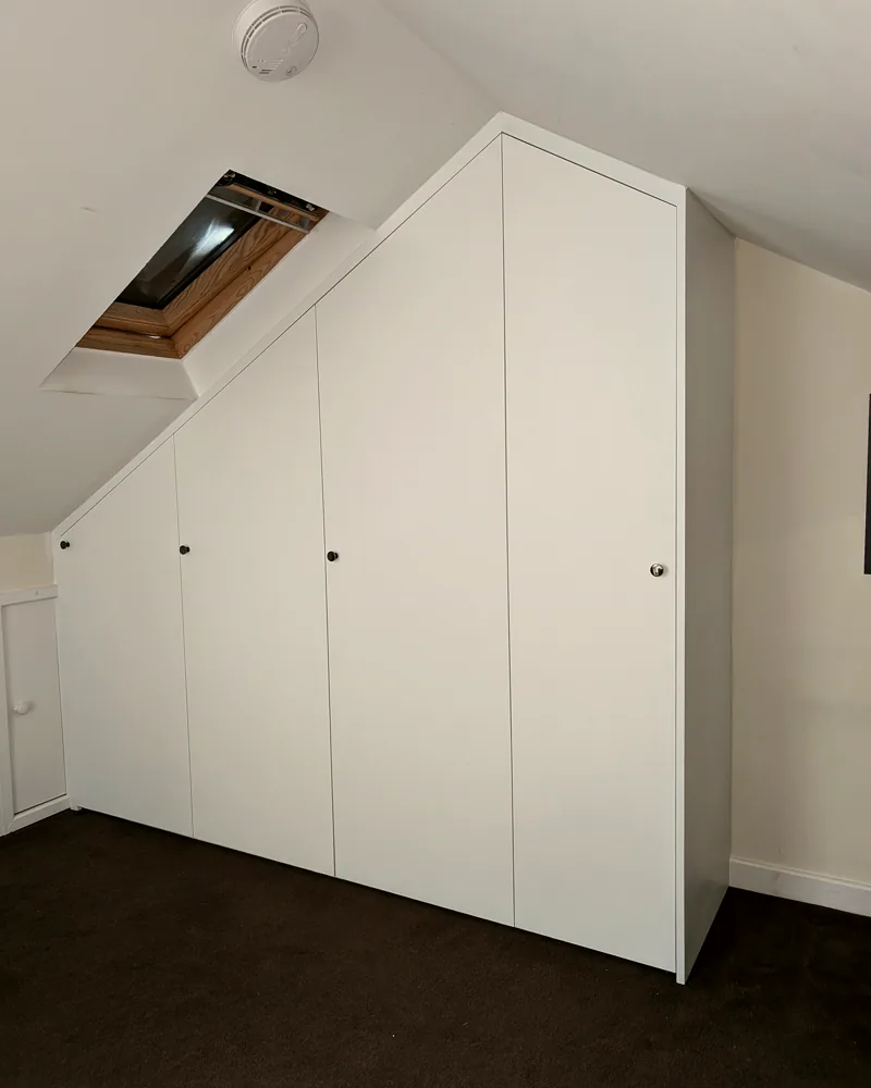White fitted wardrobes scribed to a sloping loft ceiling beside a velux window