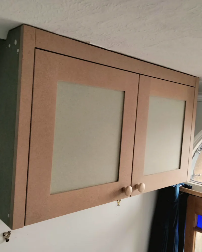 Primed cupboard built over a fuse box with panelled doors, hung and waiting for paint