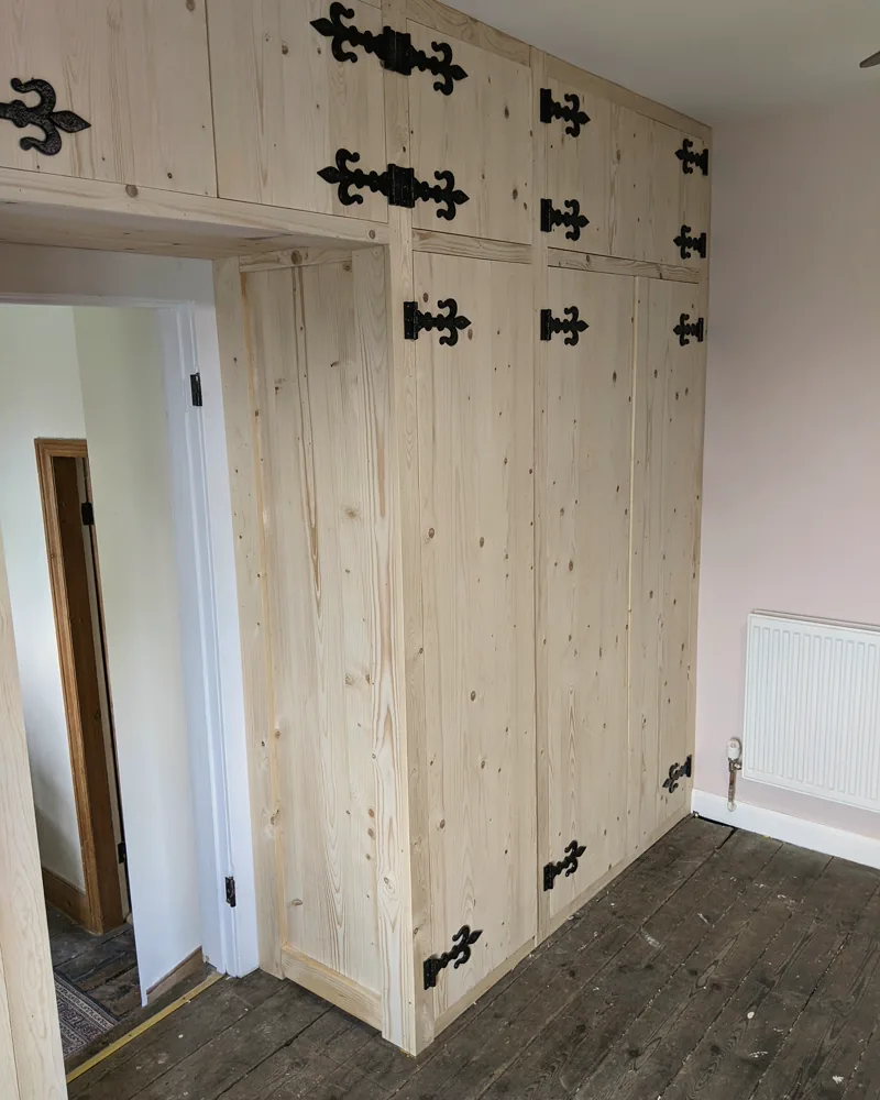 Pine fitted wardrobes with black wrought-iron hinges and a bridging unit over the doorway