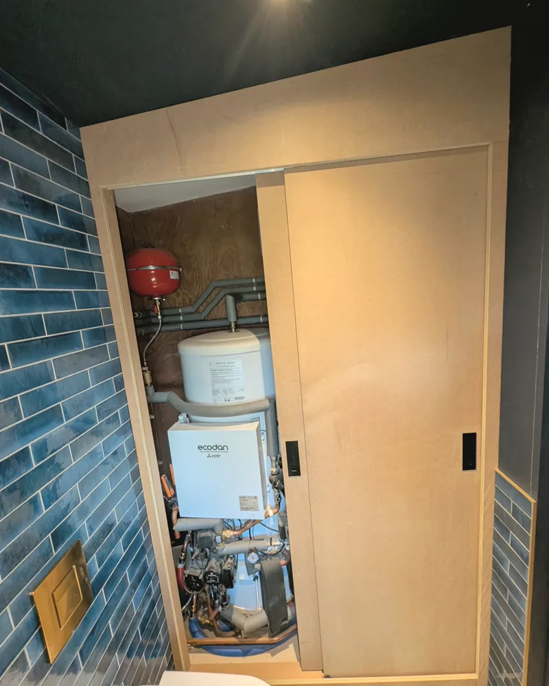 Birch faced plant room cupboard with a sliding door beside blue tiling