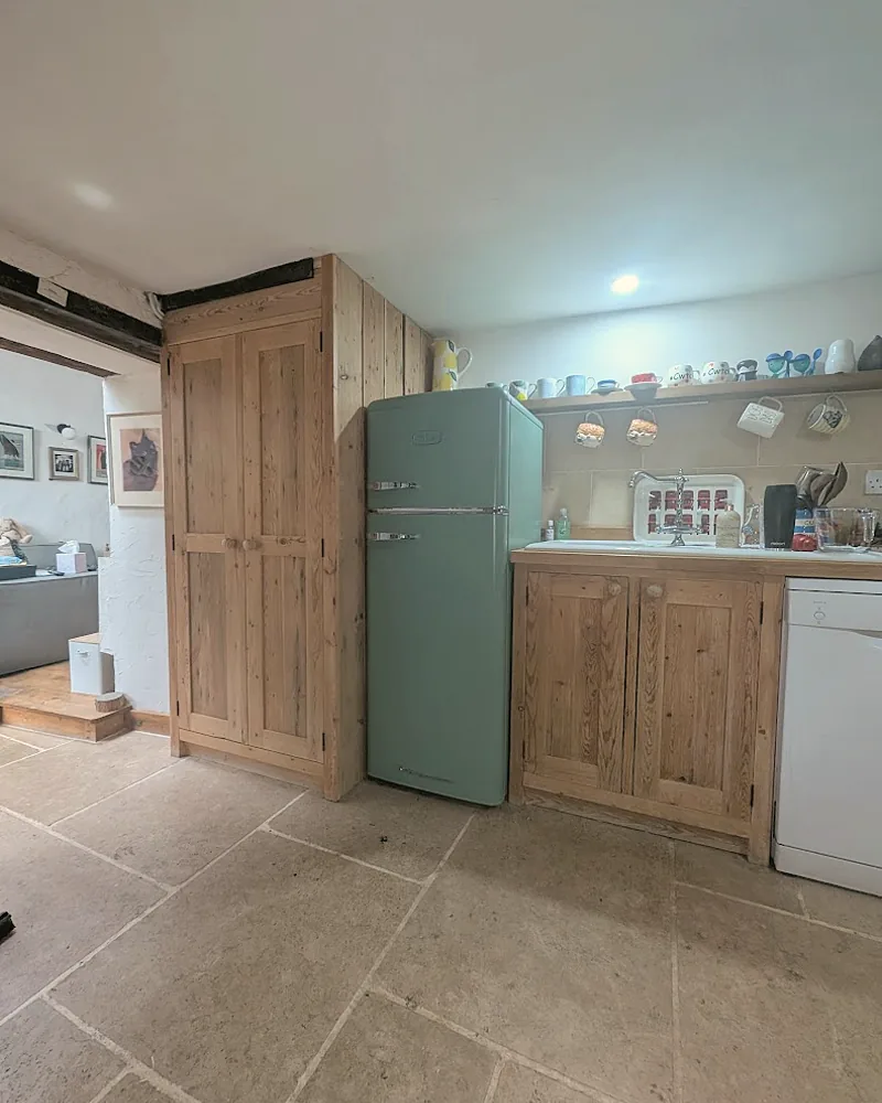 Rustic oak kitchen cupboards built around a freestanding fridge on a flagstone floor