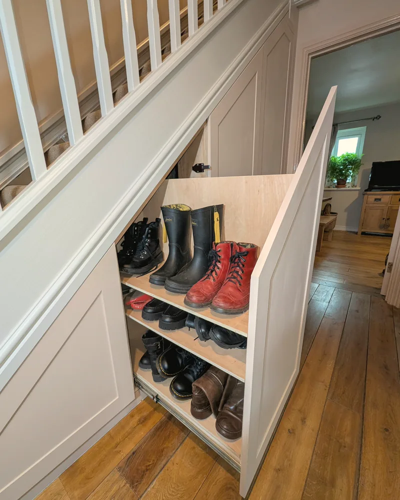 Pull-out under-stairs boot drawer open in a panelled hallway