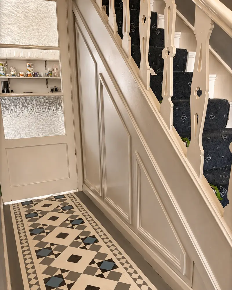 Panelled under-stairs storage in a period hallway with Victorian tiles