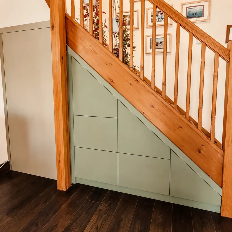 Sage-green under-stairs storage fitted beneath an oak staircase in a Hay-on-Wye home